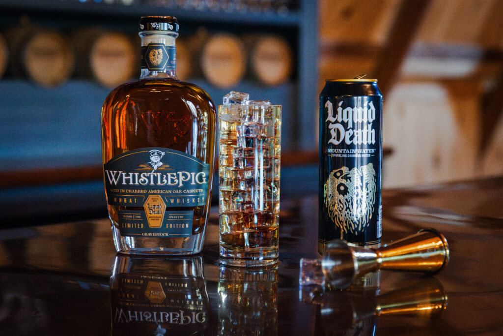A bottle of WhistlePig Whiskey, a glass of ice, a can of Liquid Death, and a jigger sit on a bar top. Photo courtesy of WhistlePig Whiskey.